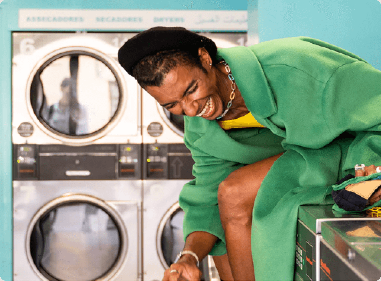 woman in green coat sitting on top of washing machine laughing 